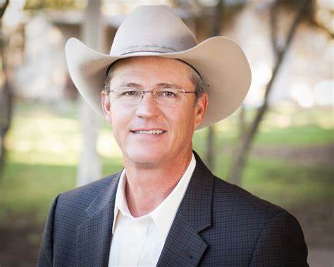 A man wearing glasses and a cowboy hat smiles. 