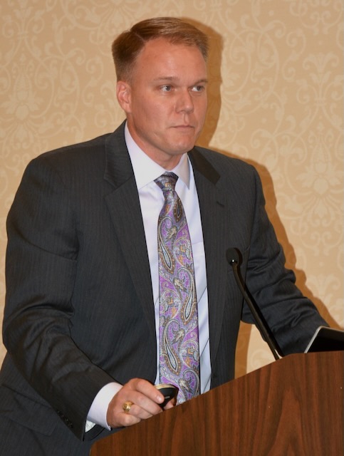 A man in a suit jacket and tie stands behind a podium.
